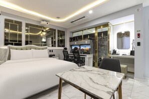 A modern hotel room with a large bed, a marble-topped table, a desk with two gaming stations, and a minibar. - Hotel felice (Daegu)