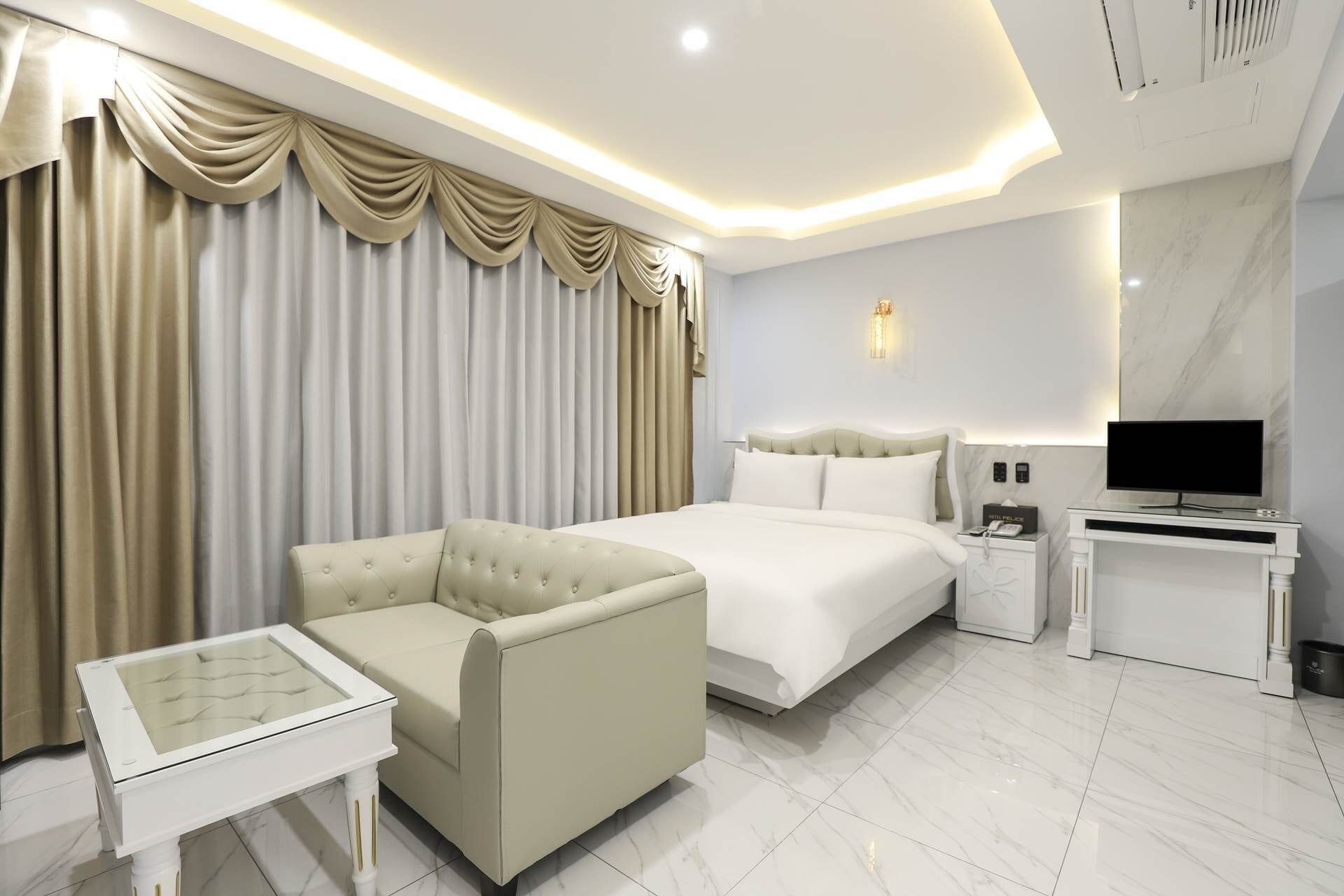 A hotel room with a bed, a sofa, a TV, a bedside table, and a lamp.