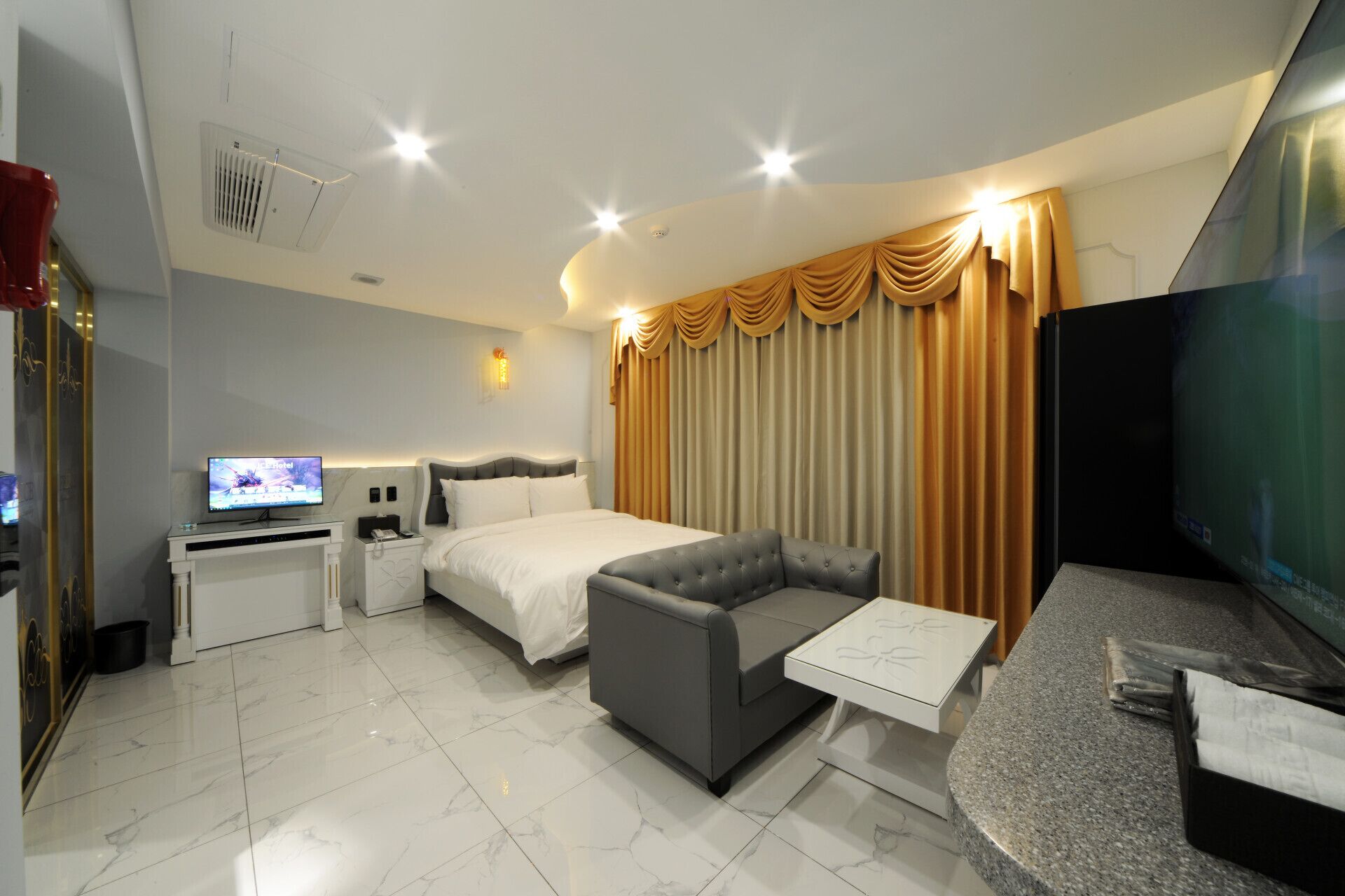 Una habitación de hotel moderna con cama, sofá, televisor, escritorio y cortinas.