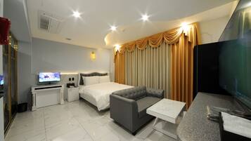 Una habitación de hotel moderna con cama, sofá, televisor, escritorio y cortinas.
