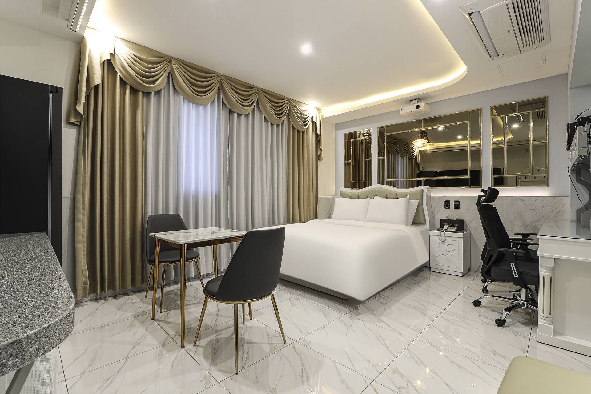 Una habitación de hotel moderna con una cama, un escritorio, una silla y un ventanal con cortinas.