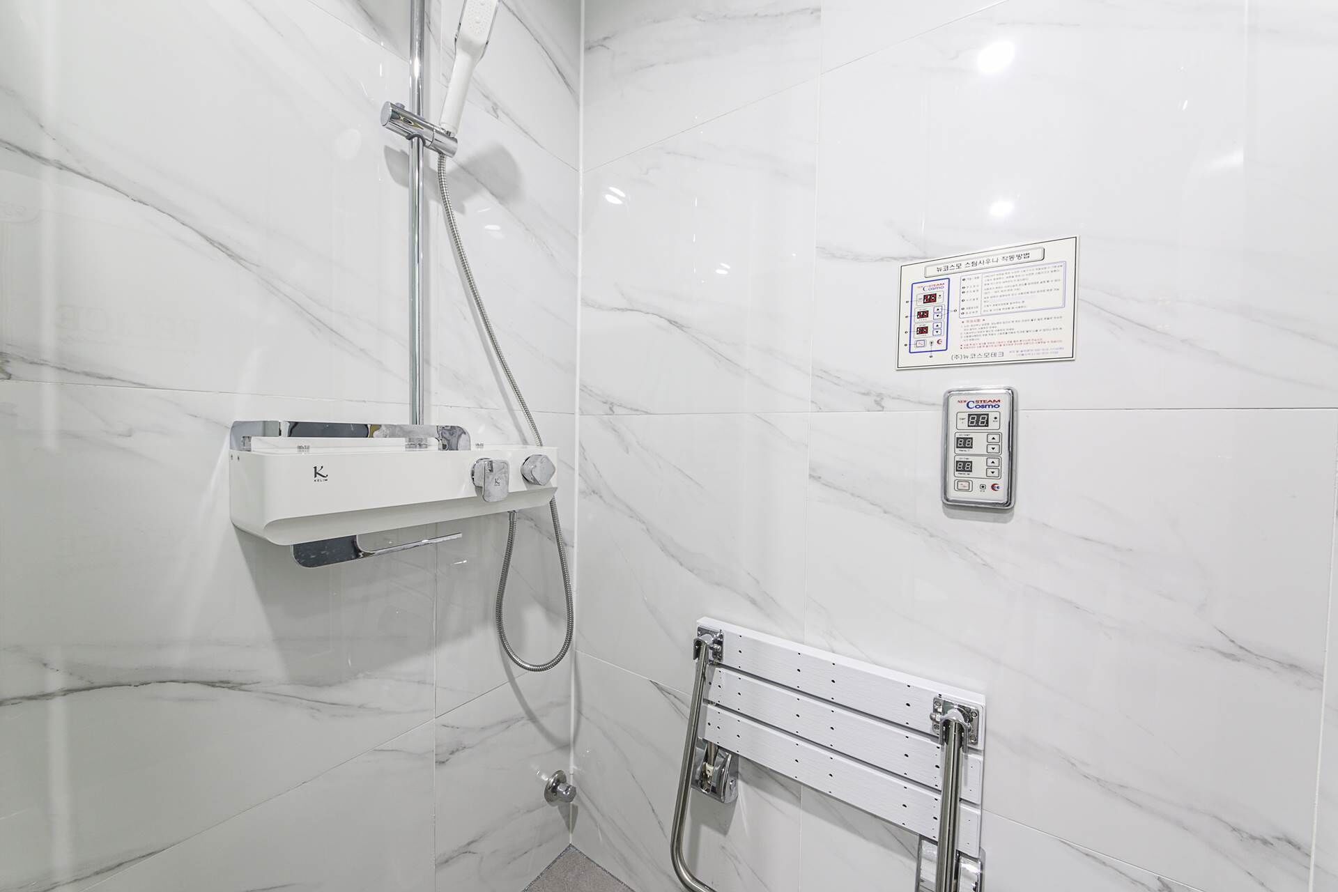 A bathroom with a shower, a control panel, and a handrail.