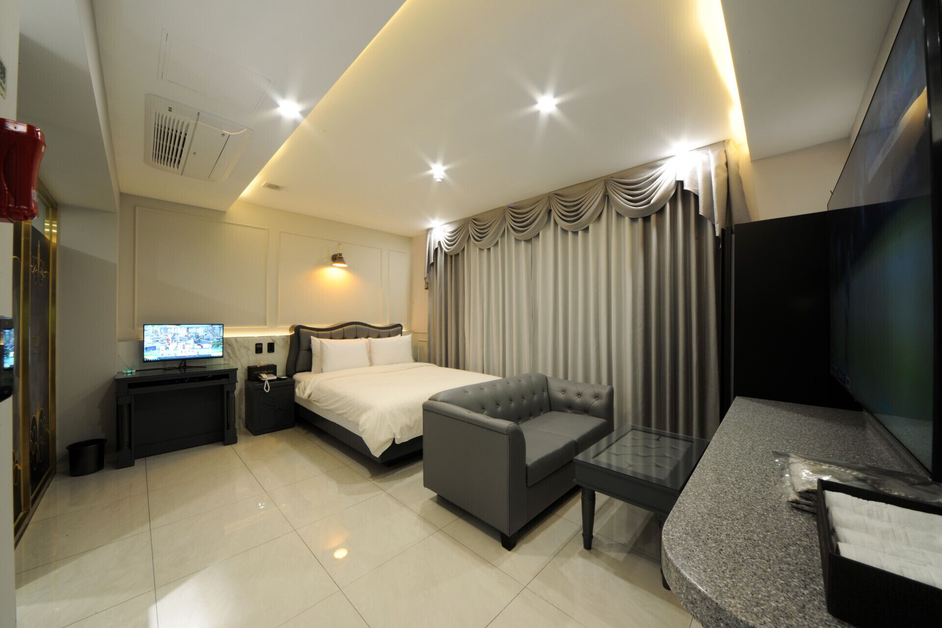 A modern hotel room with a bed, a sofa, a TV, and a desk.
