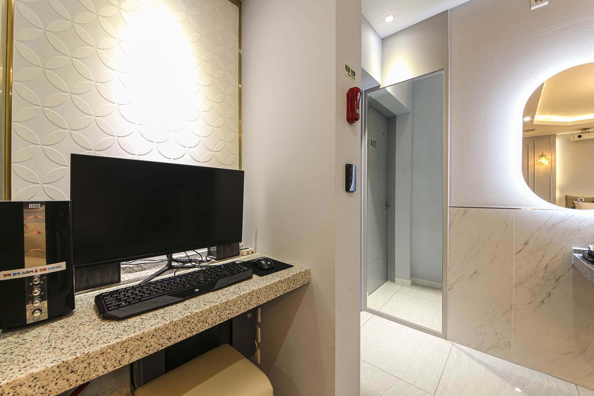 Una habitación de hotel moderna con televisión de pantalla plana, una computadora de escritorio, un teclado, una mesita pequeña y un banco.