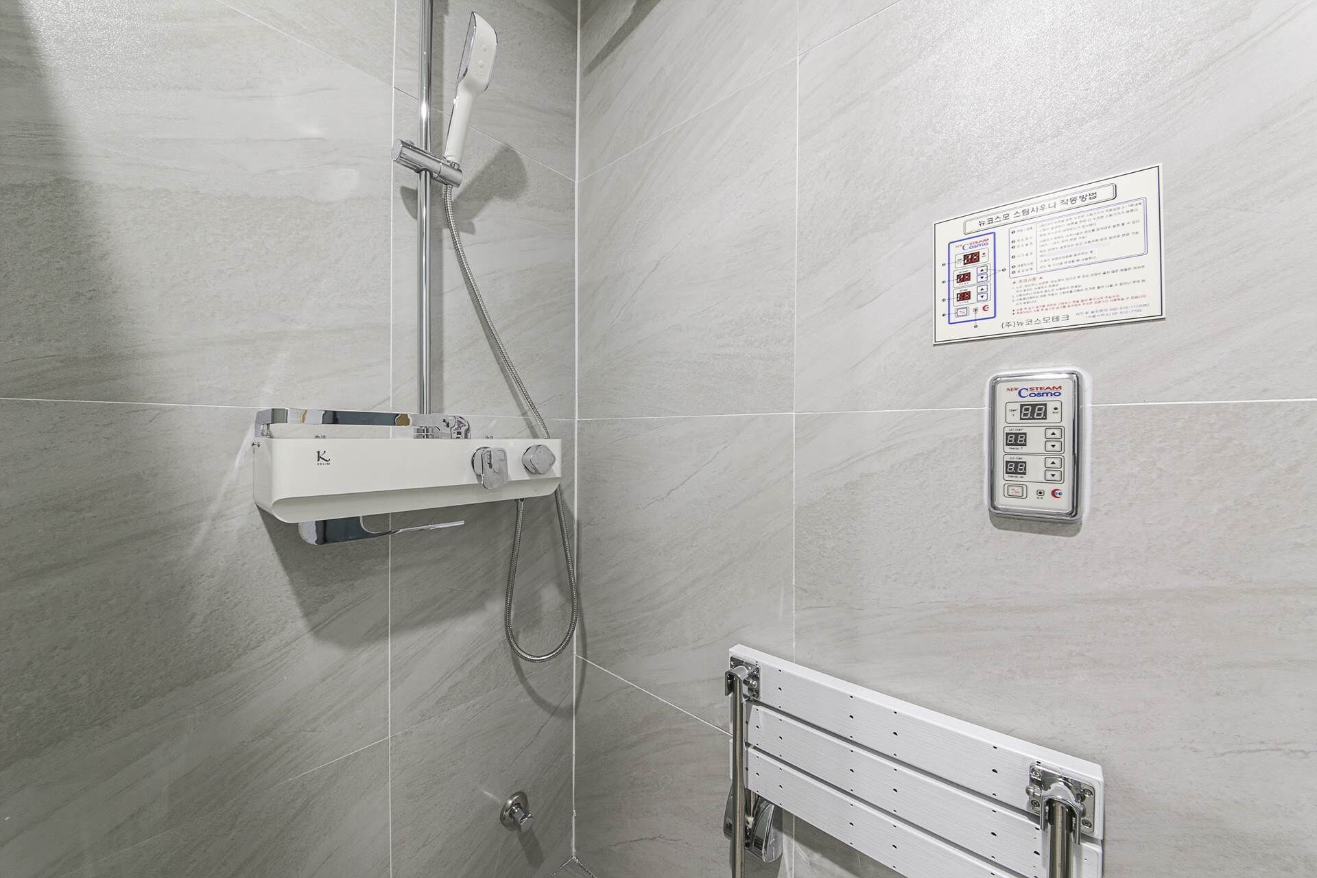 A shower with a control panel, a wall-mounted sign, and a handrail.