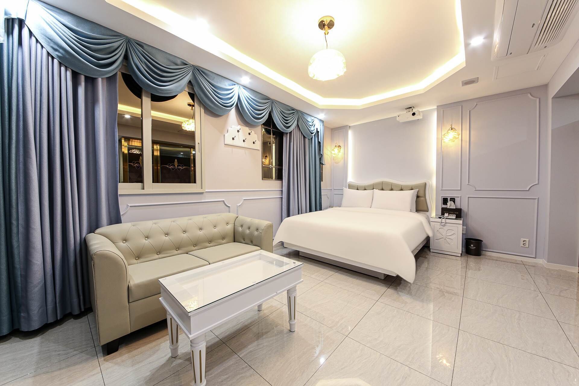 A modern hotel room with a bed, a sofa, a bedside table, and a nightstand.
