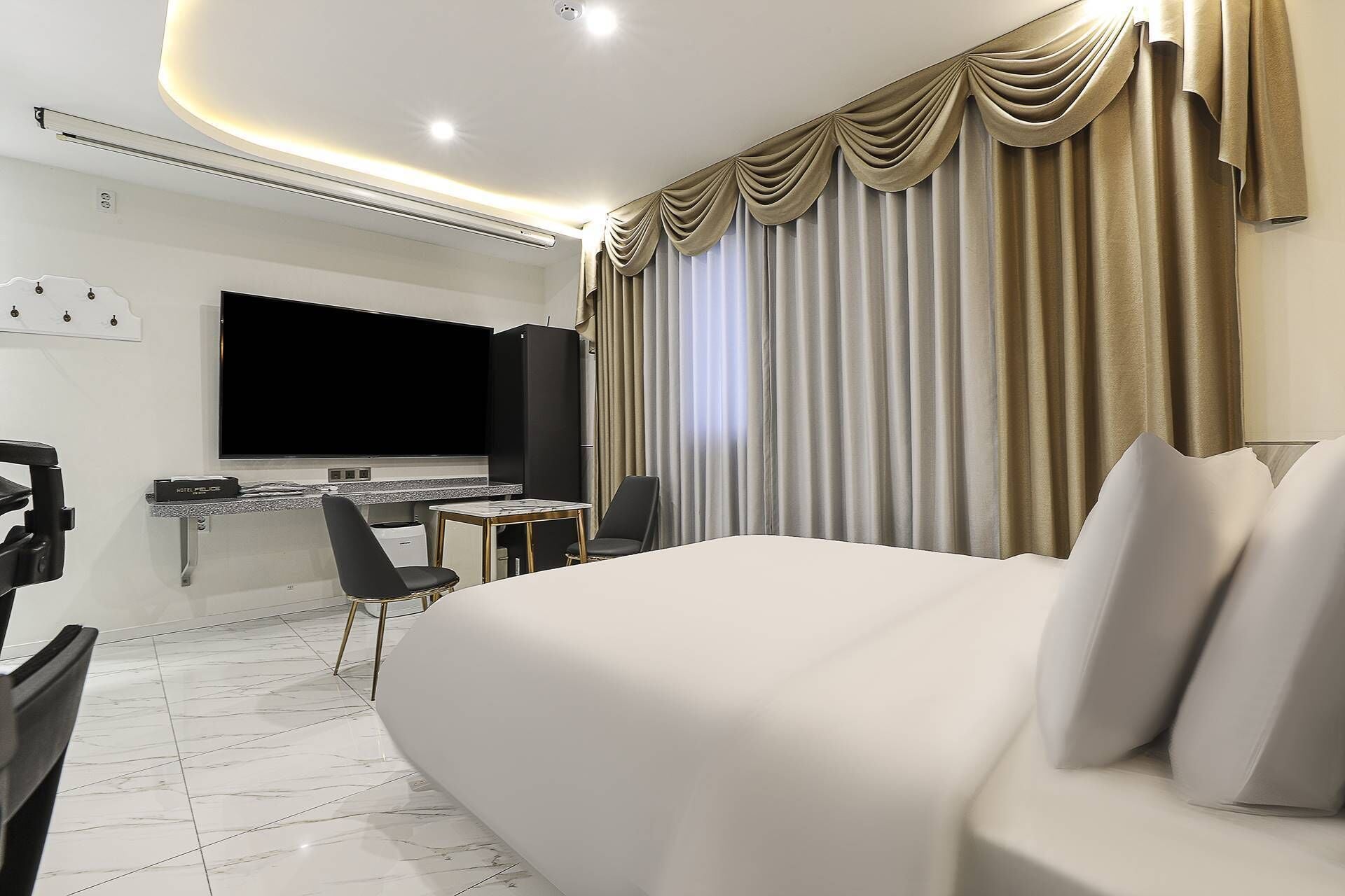Una habitación de hotel moderna con una cama grande, un escritorio con televisor de pantalla plana, una silla y un minibar.