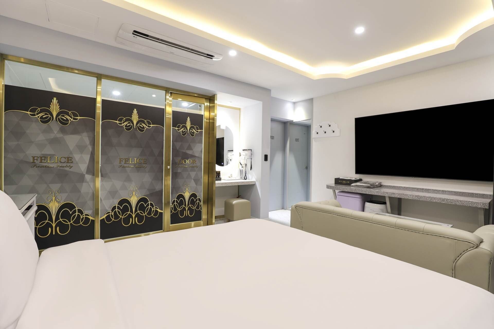 Quarto de hotel moderno com uma cama grande, televisão, escrivaninha e guarda-roupa com portas espelhadas.