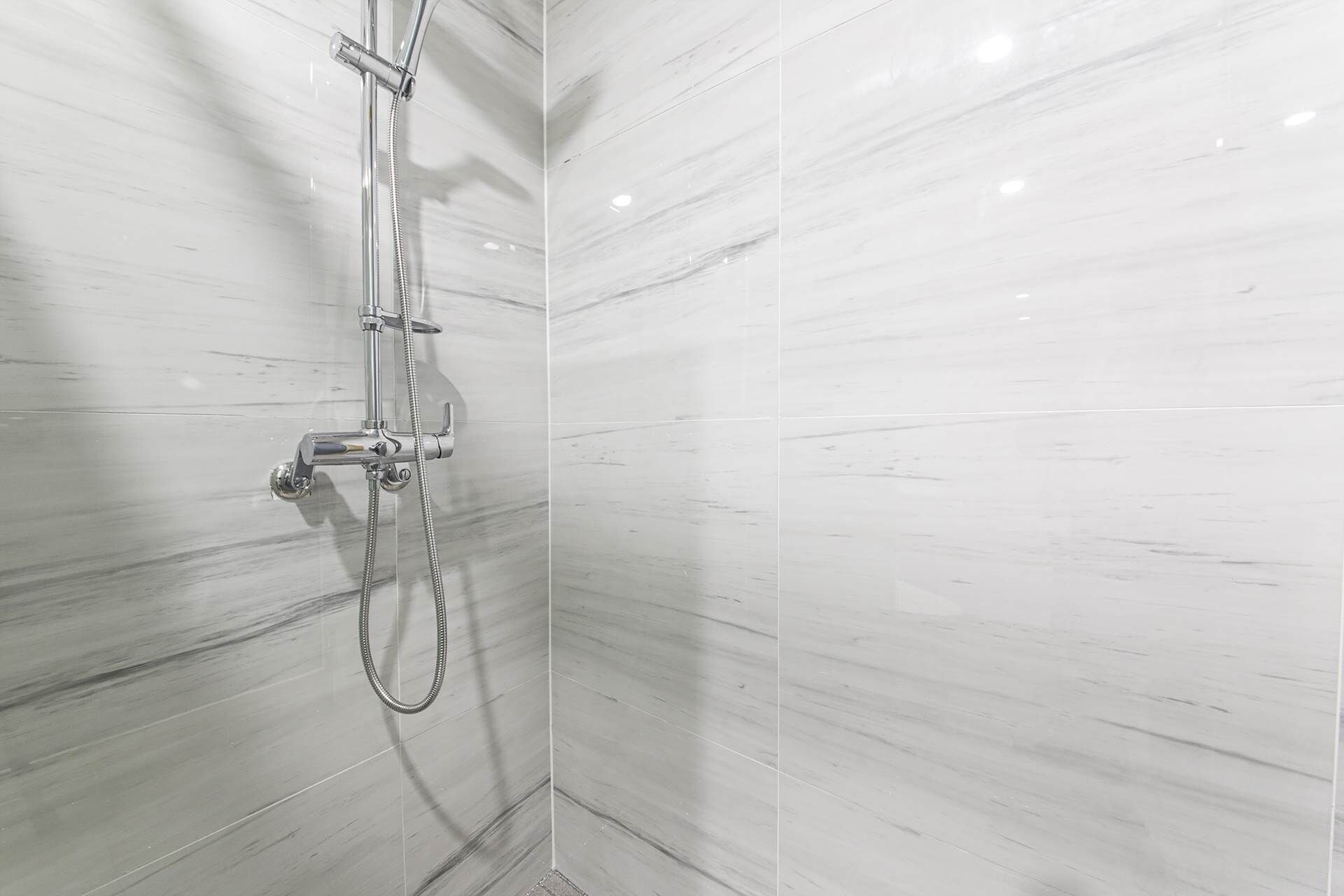 A shower with a handheld showerhead and a wall-mounted faucet.