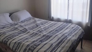 A bedroom with a bed, a window with curtains, and a plain wall. - Tranquil 1-bedroom house with AC in charming Tucson (Tucson)