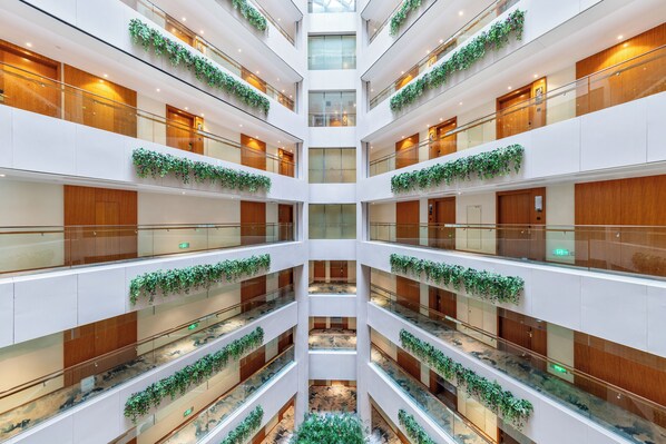 A multi-level atrium with glass railings, wooden paneling, and green plants.