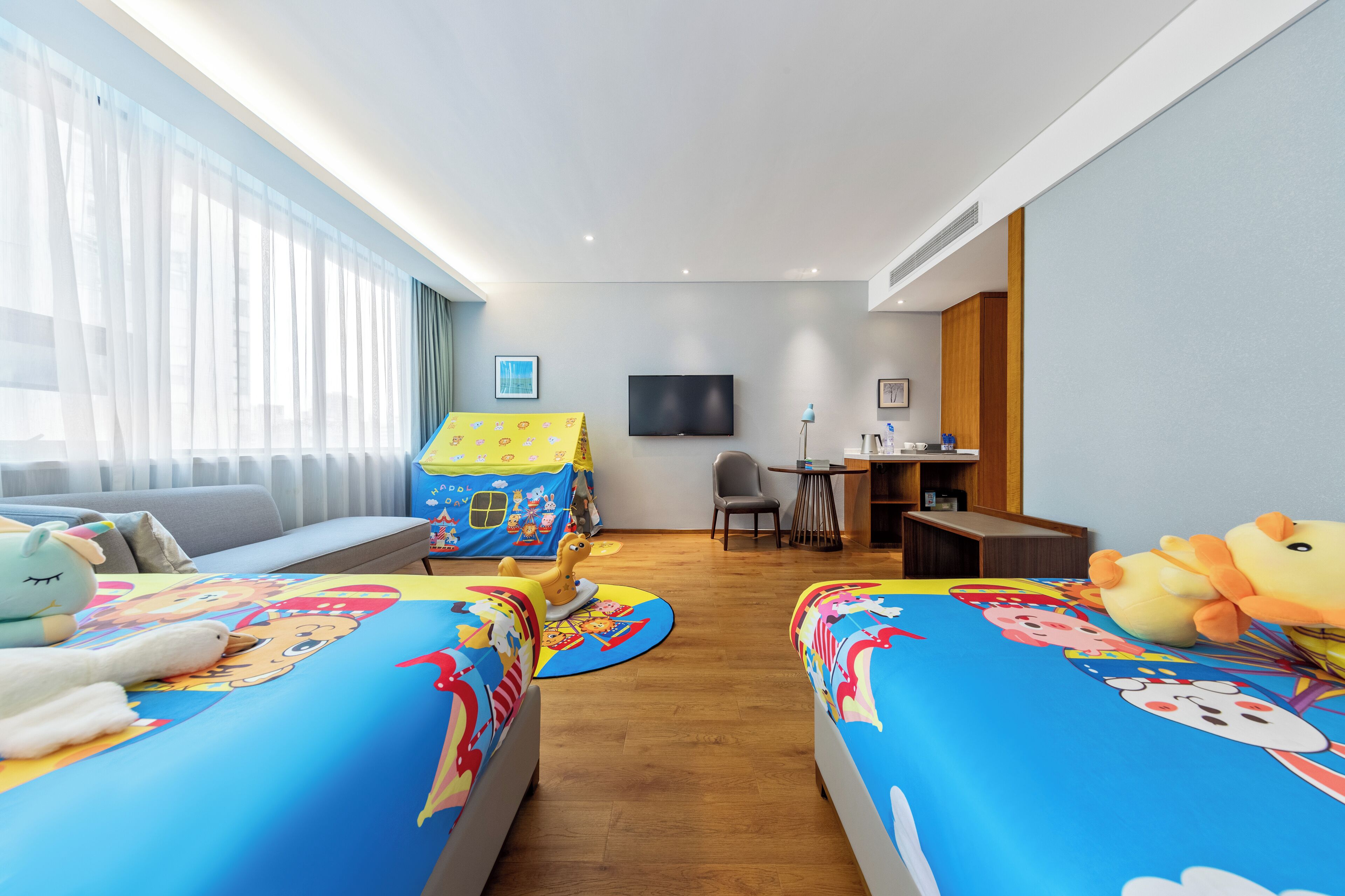 A hotel room with two beds, a desk, a chair, a TV, and a window with curtains.