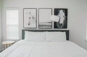 Ein Schlafzimmer mit einem Bett, weißer Bettwäsche, einem runden Beistelltisch und drei gerahmten Bildern von Pferden an der Wand.