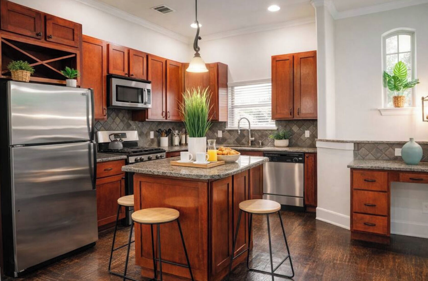 A kitchen with wooden cabinets, stainless steel appliances, a central island with stools, and potted plants.