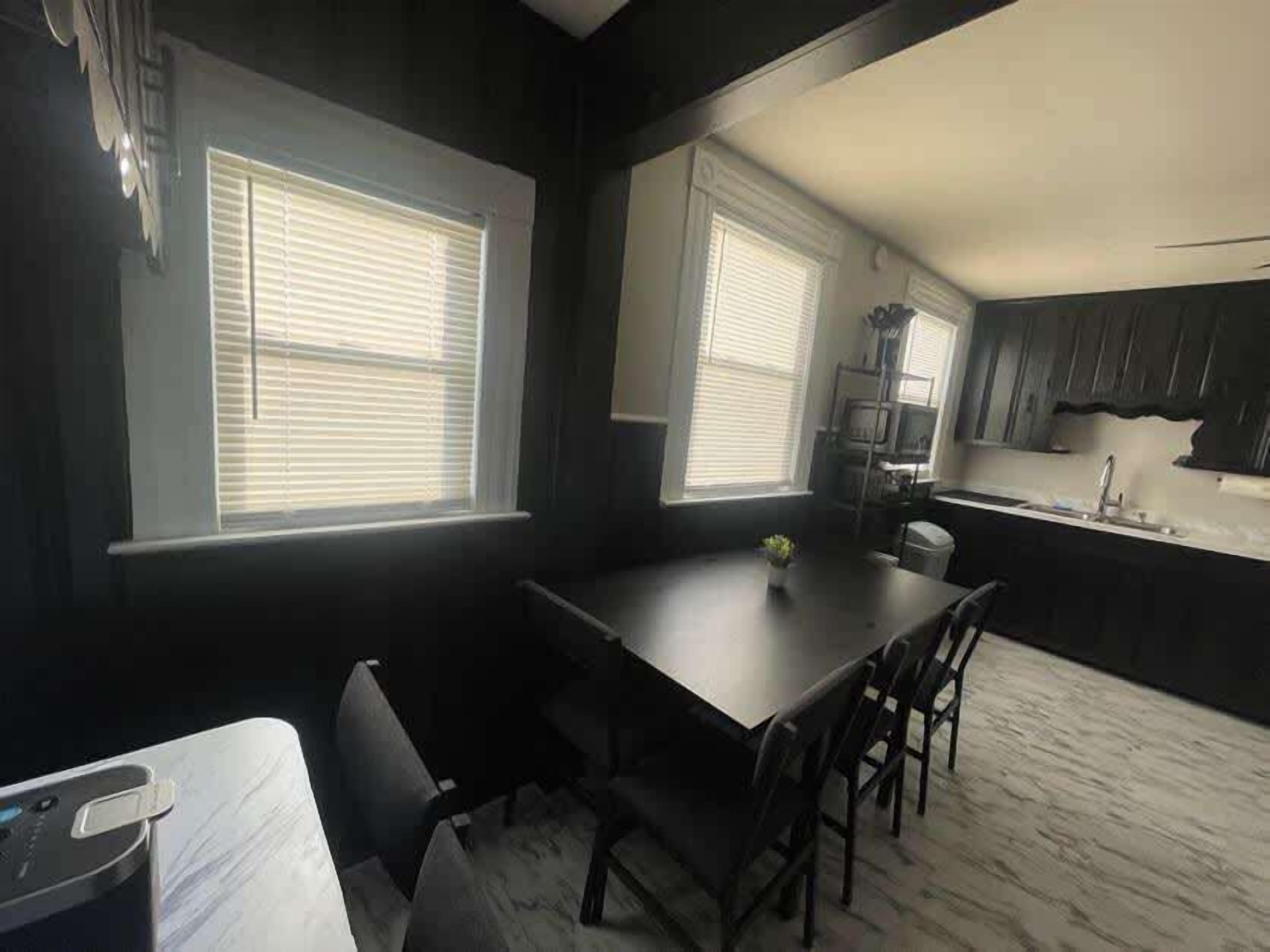 A modern kitchen with dark cabinetry, a dining table, and two windows with blinds.