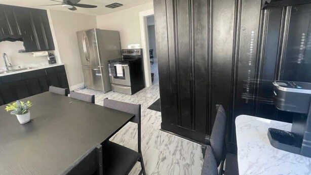 Una cucina moderna con mobili scuri, un piano di lavoro in marmo e un'area pranzo con tavolo e sedie.