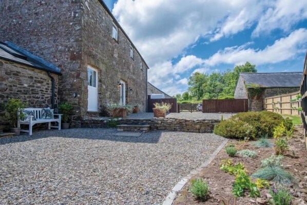 A stone building with a gravel driveway, a bench, and a garden with various plants. - The Granary - 3 Bed Barn Conversion - Llawhaden (Llawhaden)
