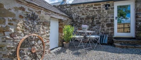 A stone building with a gravel courtyard, a wheel, and a door.