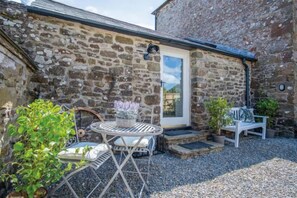 A stone building with a door, a round table with chairs, and potted plants. - The Granary - 3 Bed Barn Conversion - Llawhaden (Llawhaden)