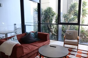 Een moderne woonkamer met een rode bank, een ronde salontafel en een stoel met een gekleurd kussen.
