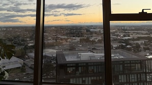 A large window with a view of a cityscape at dusk, including buildings and a clear sky.