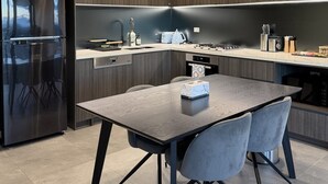 A modern kitchen with a built-in refrigerator, a dining table with chairs, and a countertop with various appliances and items.