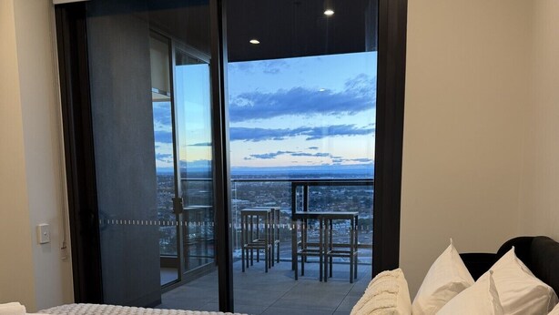 A bedroom with a bed, pillows, and a view of a balcony with chairs and tables.