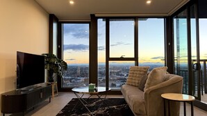 A modern living room with a large TV, sofa, and a view of a cityscape through large windows.