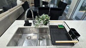 Una cocina moderna con un lavamanos de acero inoxidable, sillas negras, una planta en maceta y una bandeja negra con utensilios de cocina.