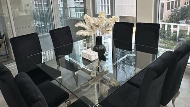 Un comedor moderno con una mesa de vidrio, sillas negras y un jarrón con flores blancas.