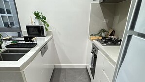 Una cocina compacta con un lavamanos de acero inoxidable, un microondas, una estufa y un cubo de basura.