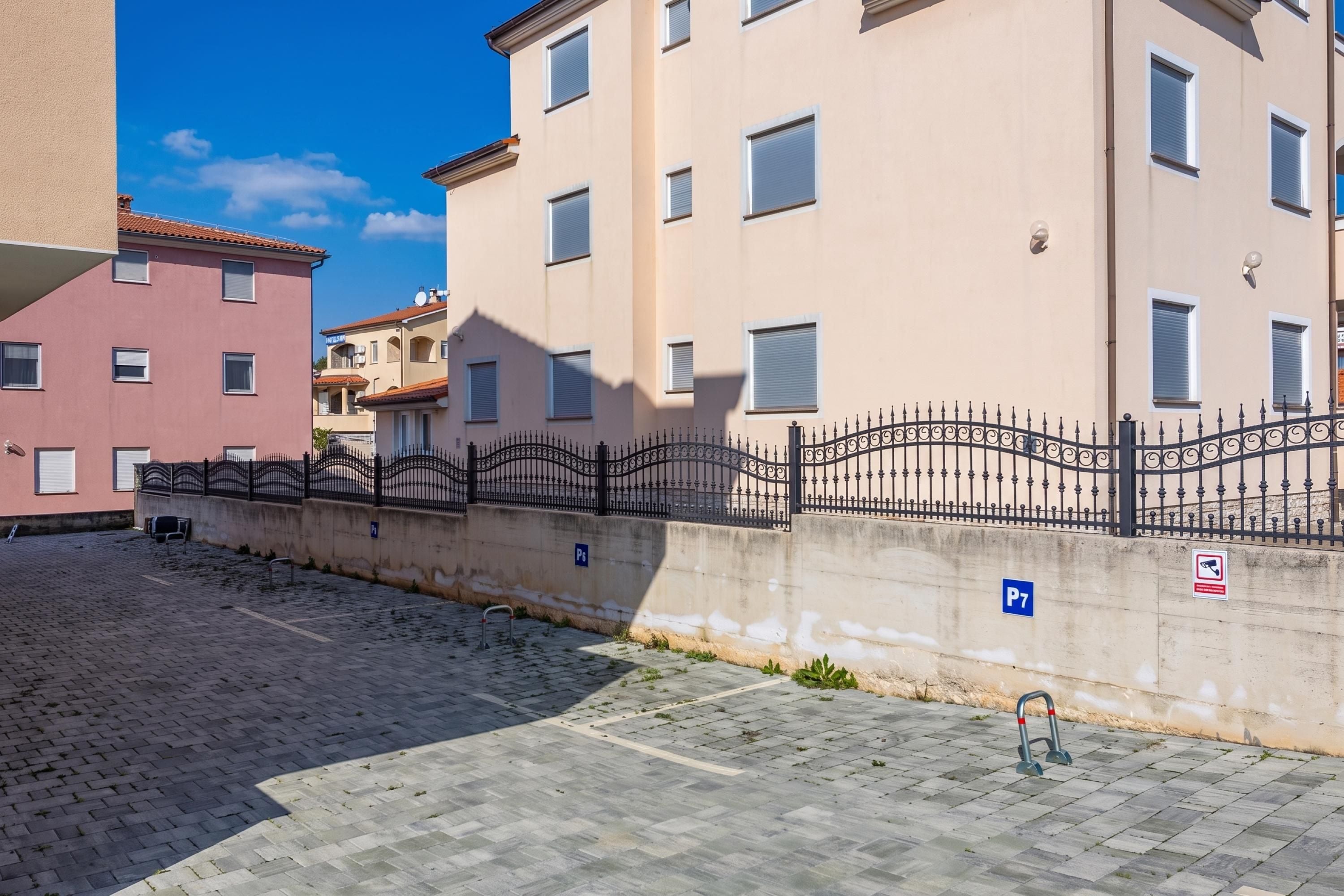 A paved street with a metal fence and a building with a flat facade and multiple windows.