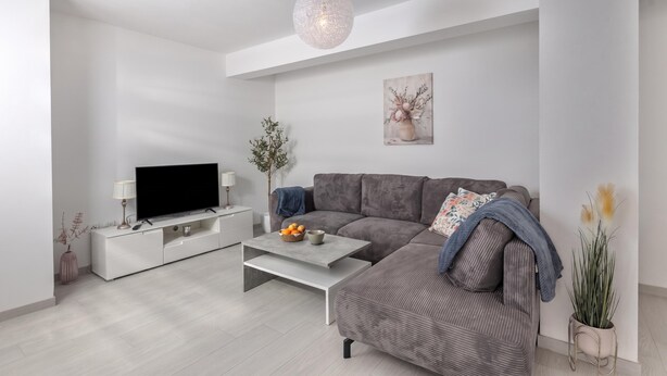 A modern living room with a grey sofa, a flat-screen TV on a white stand, a coffee table, and a hanging light fixture. - Apt Rosa Walk To Beach /w Balcony (Medulin)