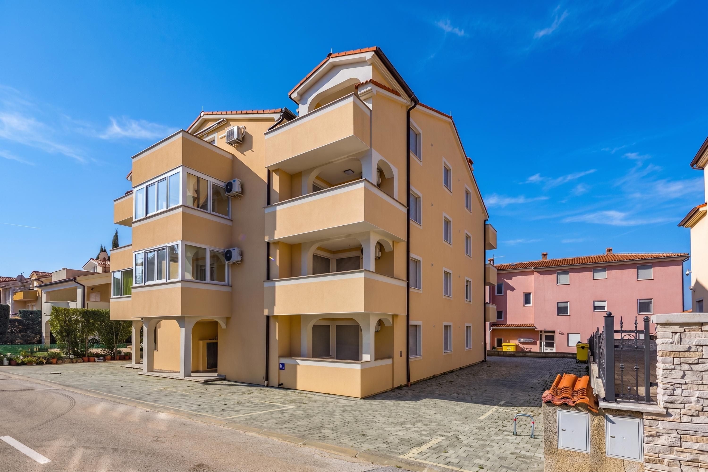 Un edificio residencial de varios pisos con balcones, un patio empedrado y un muro de piedra.