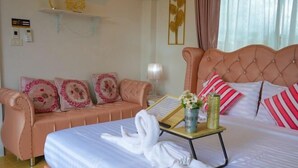 A hotel room with a bed, a sofa, a bedside table with a lamp, and a wall-mounted shelf with decorative items. - MK Land Pool Villa Khaokho (Khao Kho)