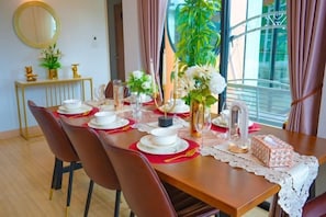 A dining area with a long table set for multiple people, chairs, a vase with flowers, and a decorative mirror on the wall.