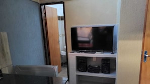 A compact living space with a television on a shelf, a small table, and a door leading to an outdoor area. - Las Lomitas Residence (Ñemby)