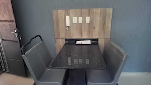 A foldable table with two grey chairs, a wooden panel with four switches, and a door to the left. - Las Lomitas Residence (Ñemby)