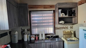 A compact kitchen with a window, a sink, a coffee maker, and a small refrigerator. - Las Lomitas Residence (Ñemby)