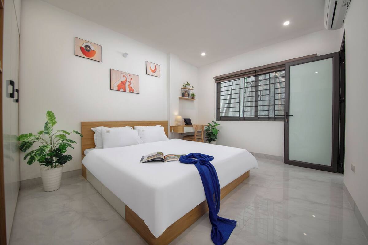 A modern hotel room with a large bed, a desk, a chair, and a window with a view.
