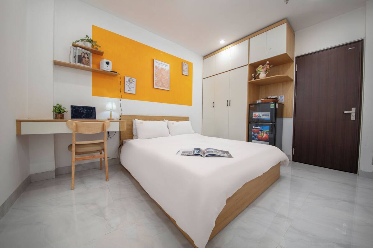 A modern hotel room with a bed, desk, chair, and wardrobe.