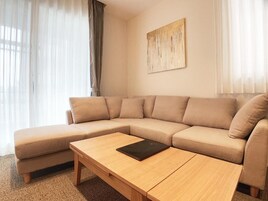 Uma sala de estar com um sofá seccional bege, uma mesa de centro de madeira e um quadro na parede.