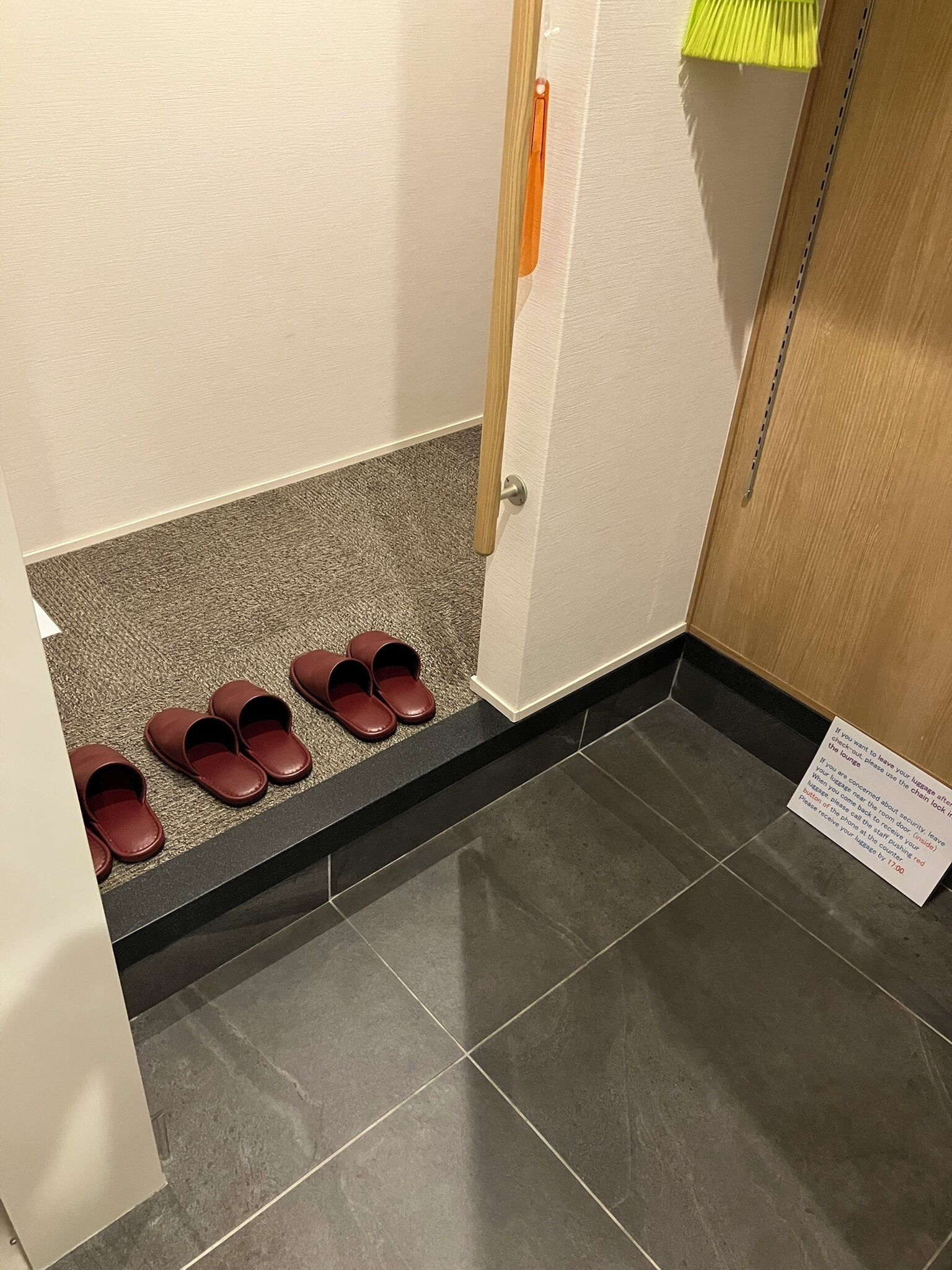 Un pasillo con un zapatero que contiene varios pares de zapatos marrones, una puerta con una cadena de seguridad y un letrero con instrucciones.