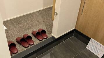 Un pasillo con un zapatero que contiene varios pares de zapatos marrones, una puerta con una cadena de seguridad y un letrero con instrucciones.