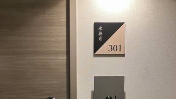 Una habitación de hotel con una puerta de madera, un letrero con caracteres japoneses y el número 301, y un lector de tarjetas de acceso.