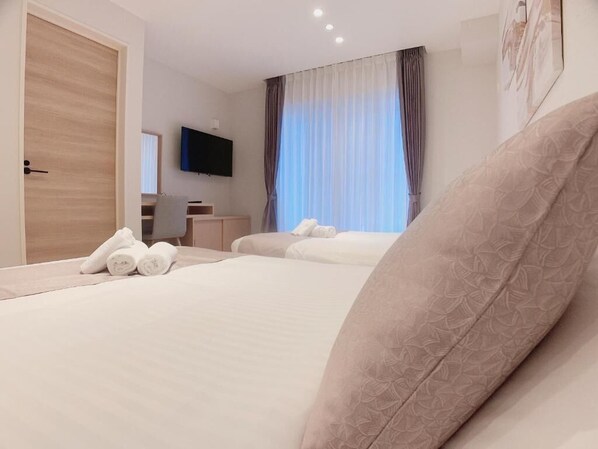 Ein Hotelzimmer mit zwei Betten, einem Flachbildfernseher, einem Schreibtisch und einem großen Fenster mit Vorhängen.