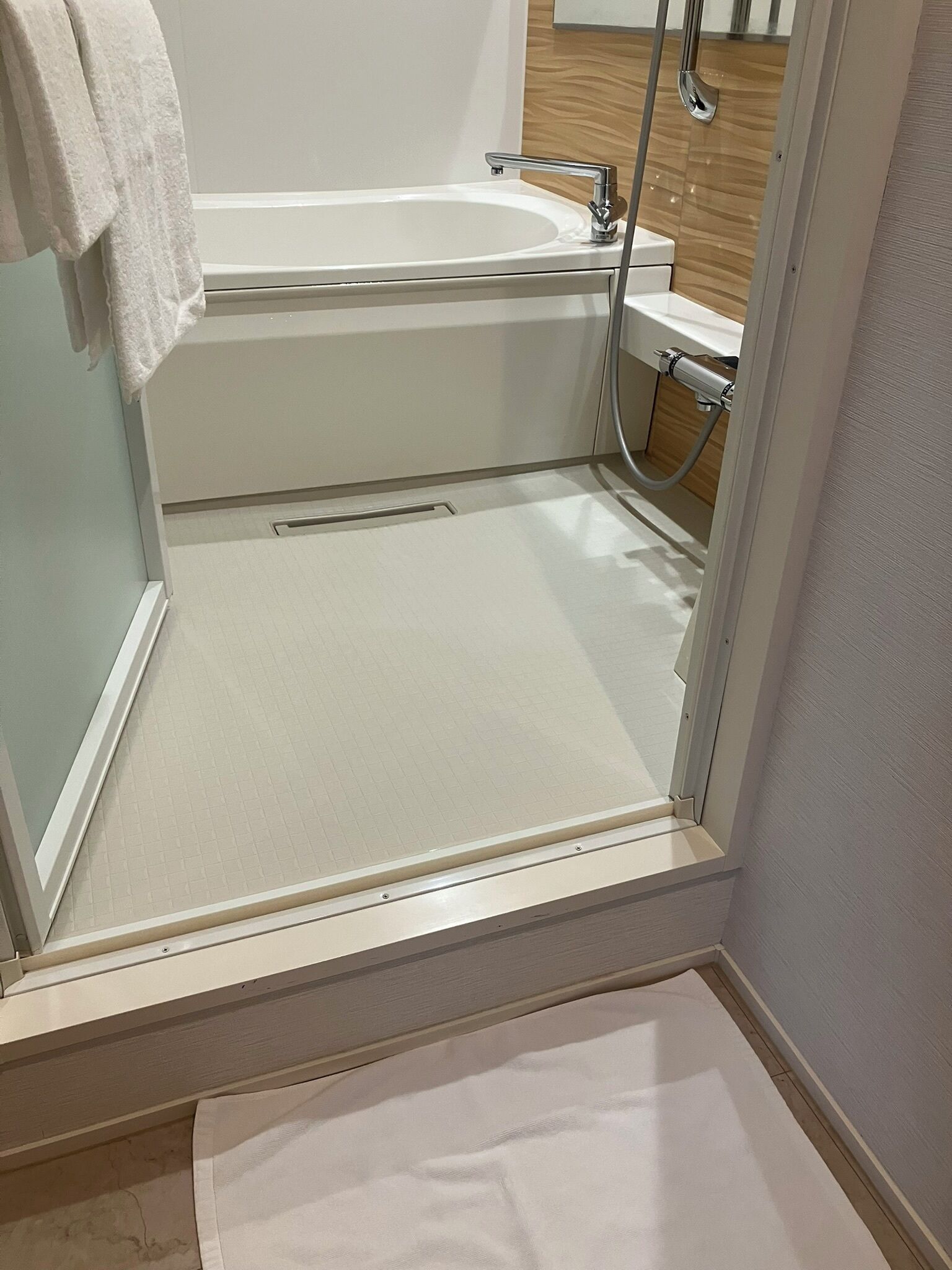 Un baño con una bañera blanca, zona de ducha y una toalla blanca colgada en la pared.