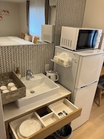 Uma cozinha compacta equipada com micro-ondas, frigorífico, pia e gavetas para arrumação.