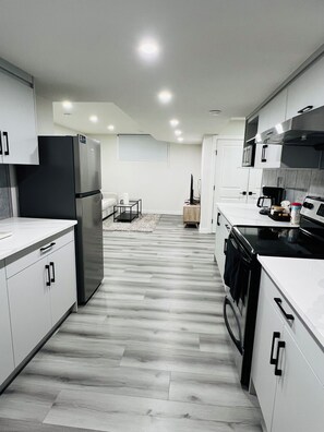 A modern kitchen with white cabinetry, a black refrigerator, a stove, and a dining area with a table and chairs.