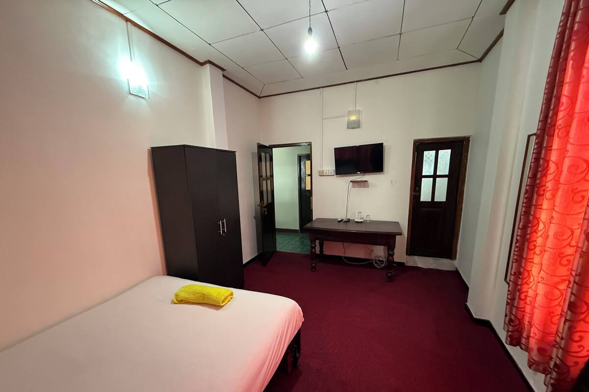 Quarto de hotel com cama, guarda-roupa, secretária, televisão e uma cortina vermelha.